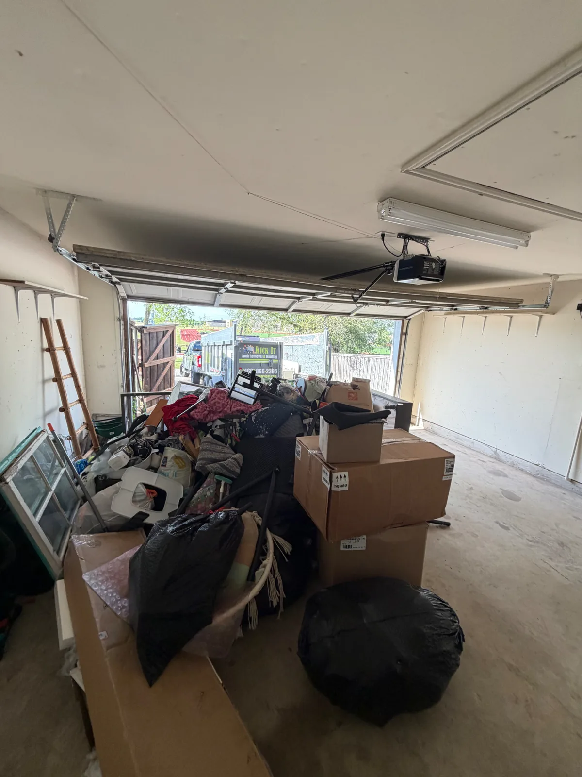 Before photo of a two-car garage packed full of boxes, bags, and household items