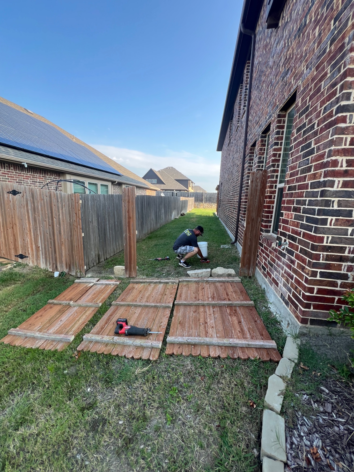 Worker removing wood privacy fence panels along a Forney side yard with panels laid out on the grass