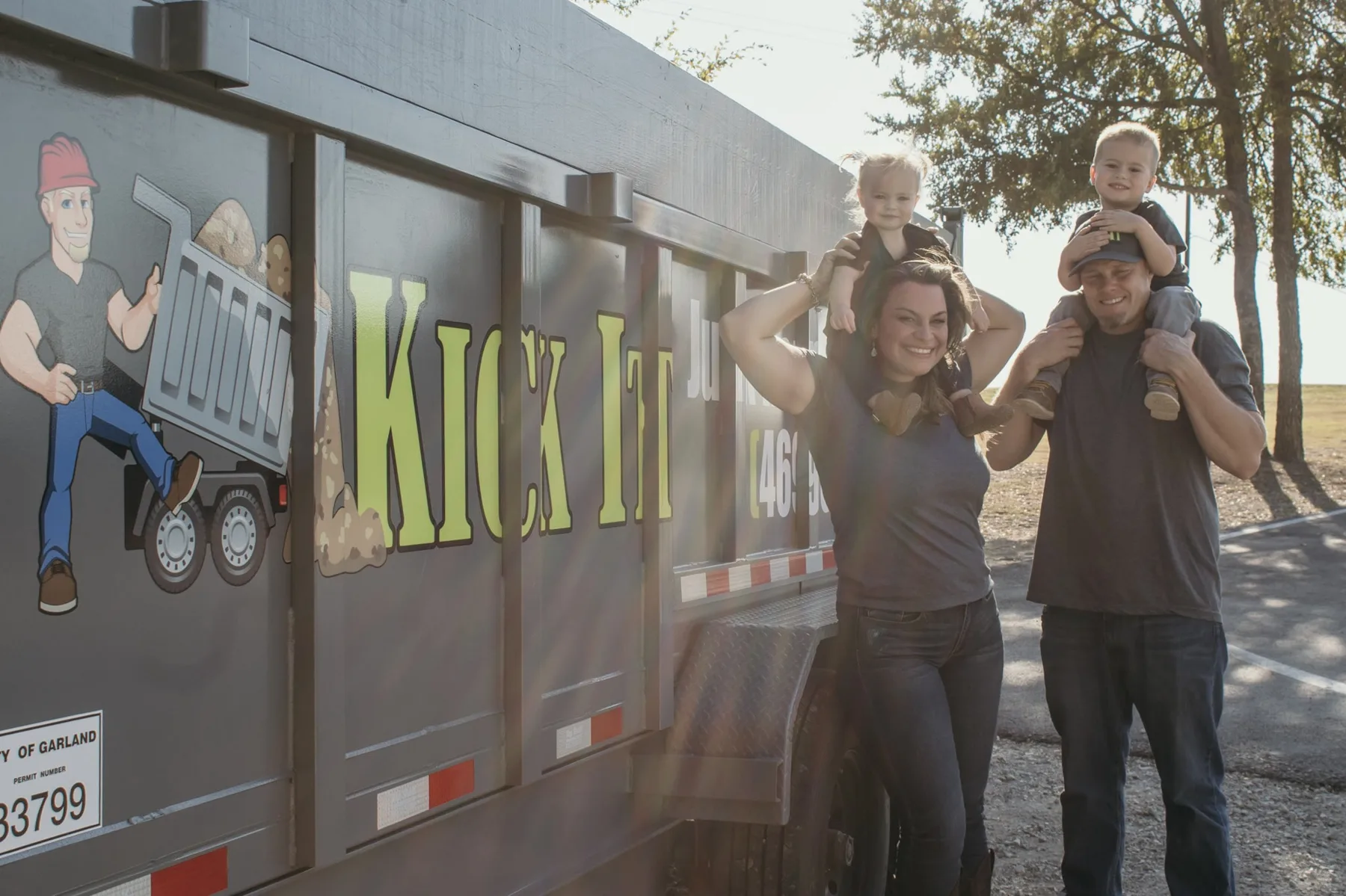 The Kick It family standing beside their junk removal trailer