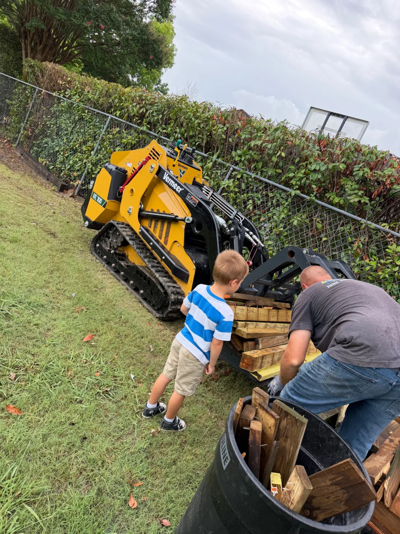 Our son watching Paul load old playset wood with the skid steer at Kick It Junk Removal